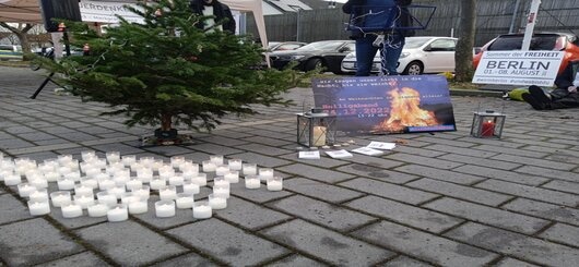 Weihnachtsbaum, rechts daneben auf dem Boden Grundgesetze, eine Laterne und ein Plakat mit der Einladung zur Demo